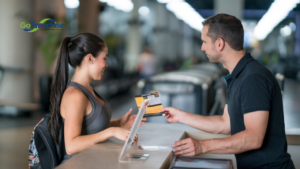 Woman with a backpack hands over a payment card to a man at a counter; GoFranchise logo visible in the background.